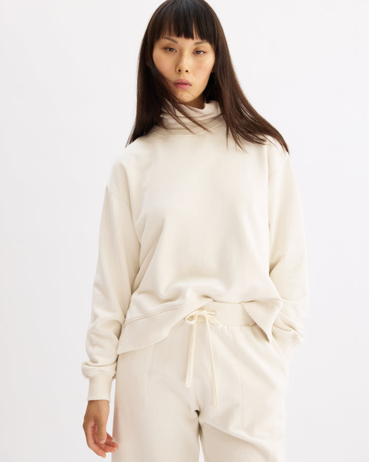 A person with long straight hair wears the Arlo Mott Delancey Crew Neck Sweatshirt in Chalk, paired with matching drawstring pants, standing against a plain white background.
