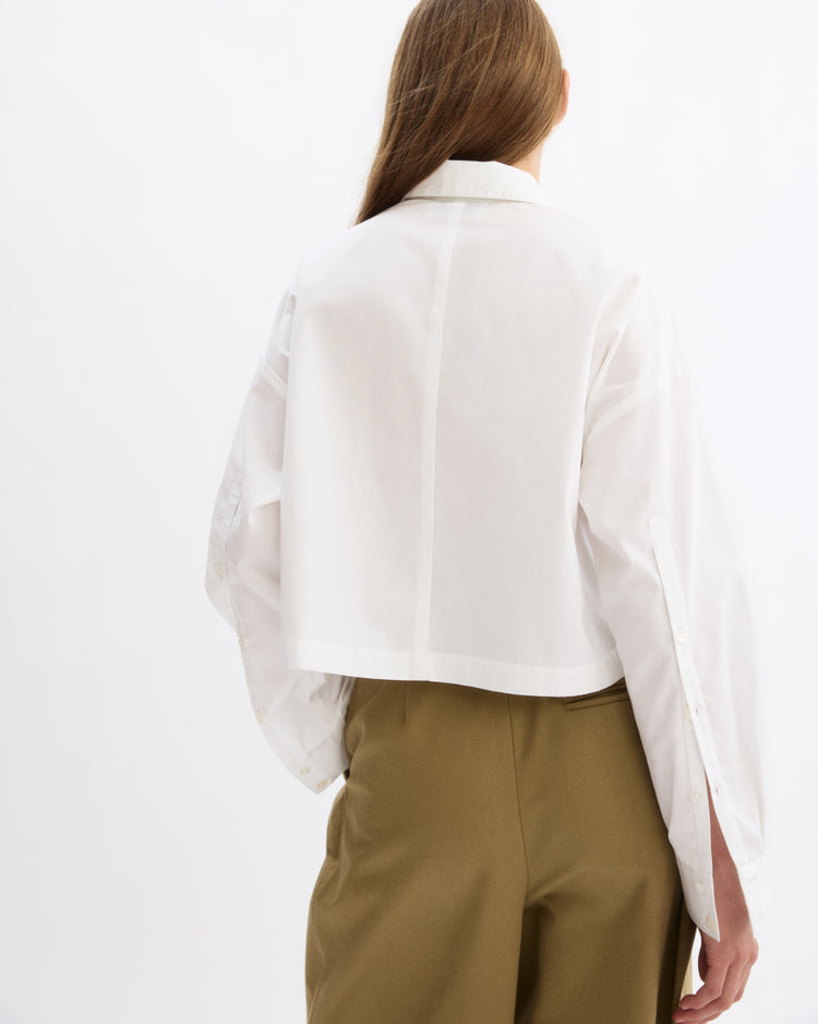 A person with long brown hair is seen from behind against a plain white background, wearing the Arlo Mott Hester Boxy Short Button Down in White and high-waisted khaki pants.