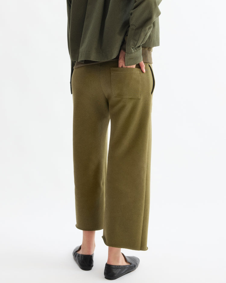 A person stands with their back to the camera, wearing Arlo Mott’s Kane Cropped Wide Sweatpants in Olive—crafted from Italian terry cloth with a visible back pocket—paired with a matching green top and black flats. Made in New York.