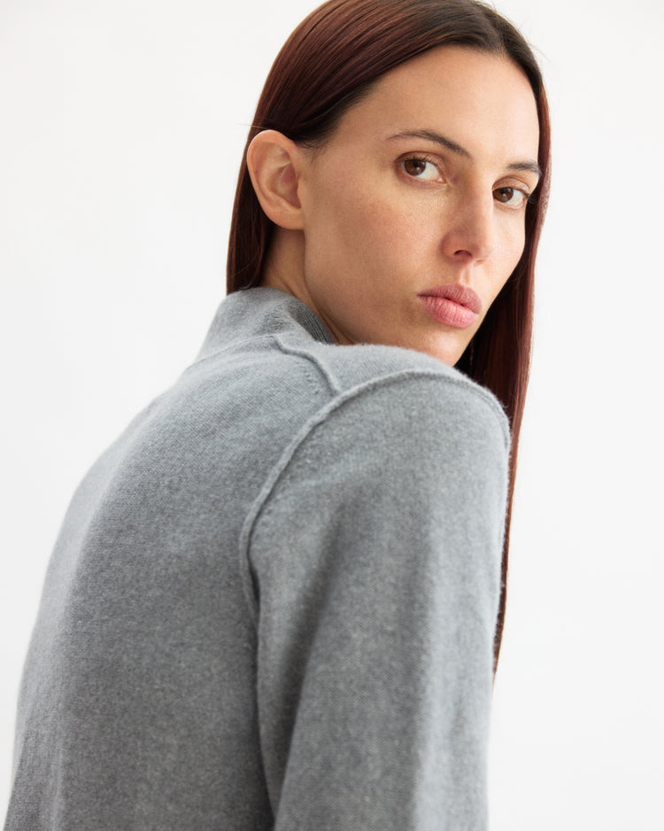 A person with straight, long brown hair wears the Arlo Mott Perry Boxy Cardigan in Heather Grey, looking over their shoulder towards the camera against a plain white background.