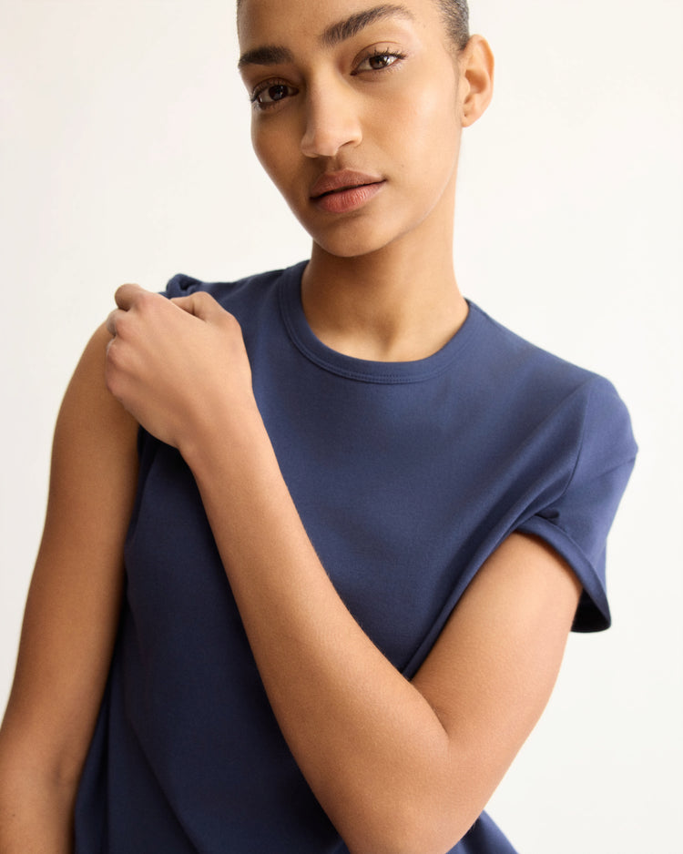 A person with short hair wears the Arlo Mott Willow Short Sleeve Tee in Navy, made in New York, looking at the camera with one hand on their opposite shoulder against a light background.