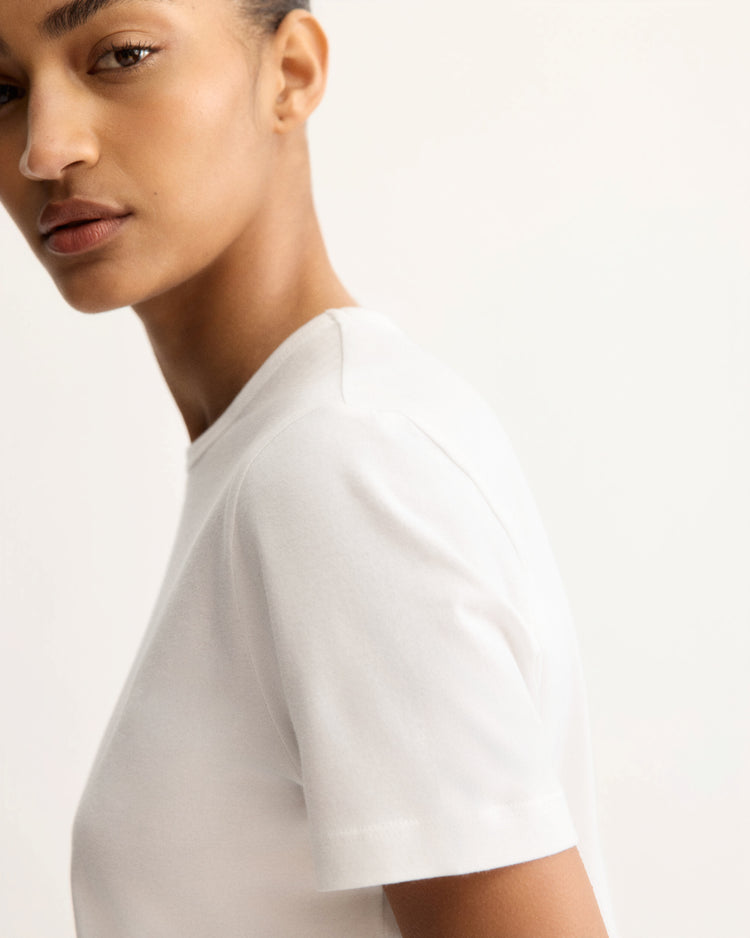 A person with short hair models the Arlo Mott Willow Short Sleeve Tee in White, shown from the side and glancing toward the camera against a neutral background.