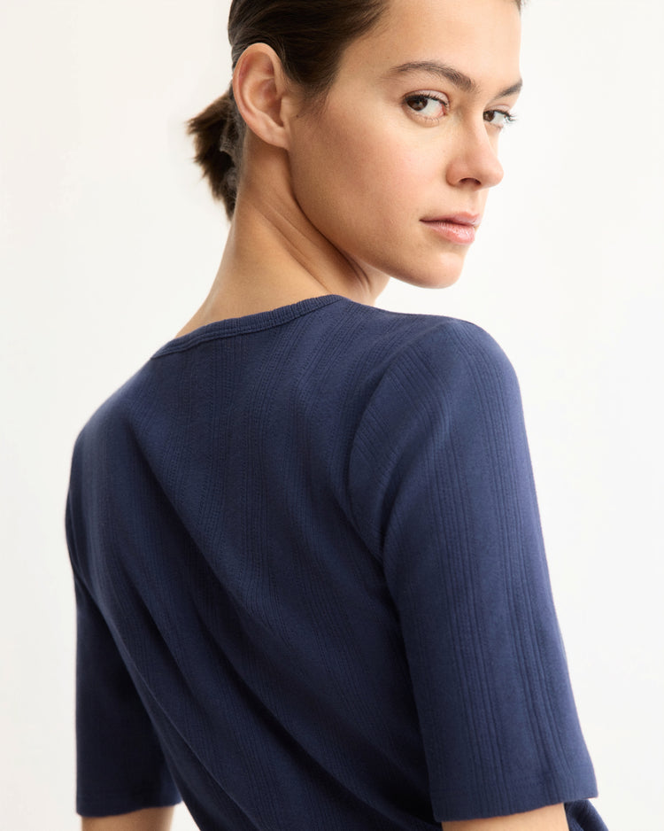 A person with short dark hair wears the Arlo Mott Quincy Slim Fit Tee in Navy, featuring a textured design, as they look over their shoulder toward the camera against a light background.