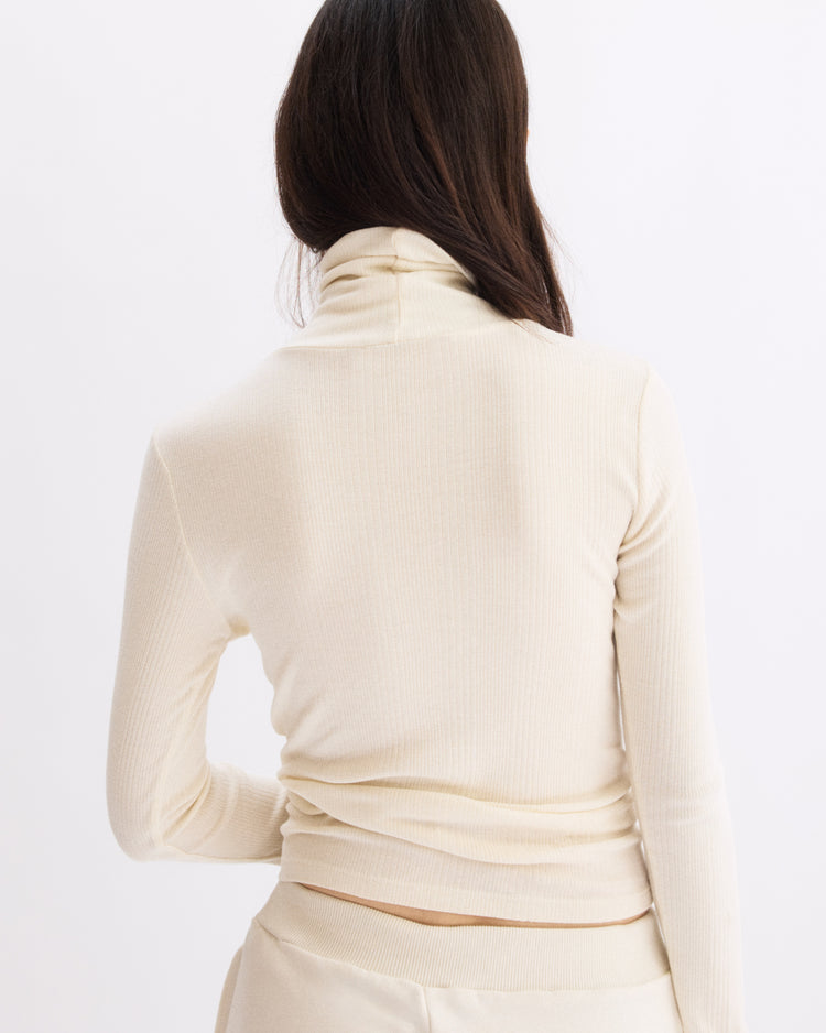 A person with long brown hair wears the Arlo Mott Clinton Long Sleeve Turtleneck in Chalk, facing away from the camera against a plain white background.