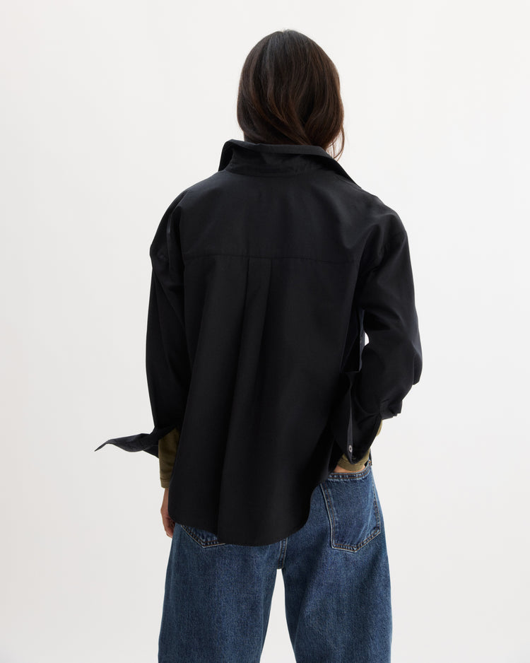 A person with long dark hair faces away, wearing the Arlo Mott Watts Side Button Shirt in Black and blue jeans against a plain white background.