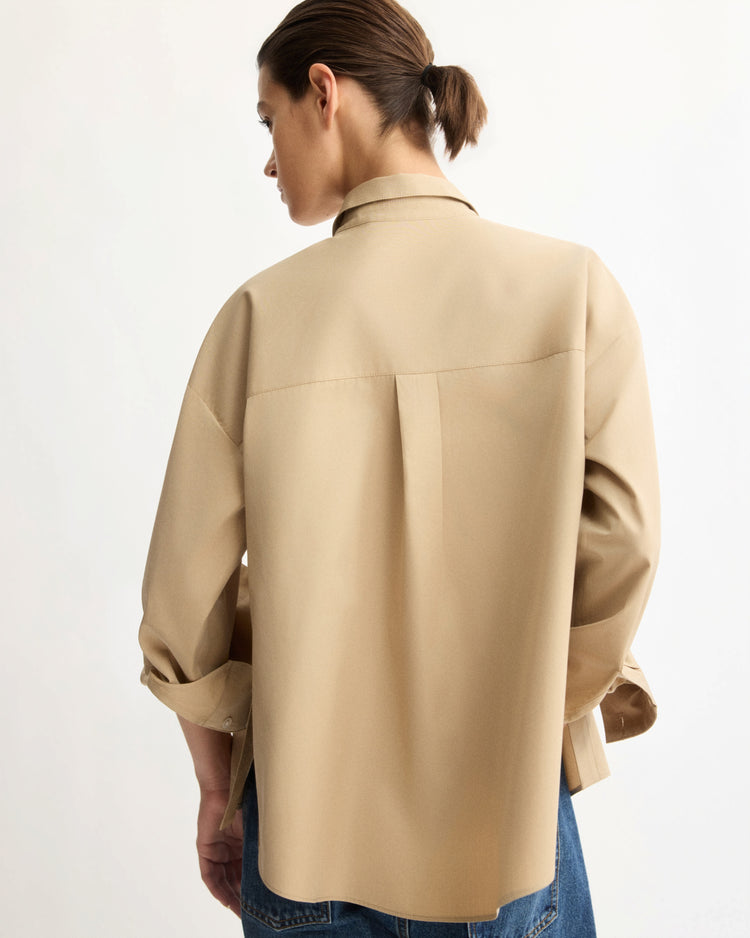 A person with brown hair tied back is seen from behind, wearing the Arlo Mott Watts Side Button Shirt in Khaki and blue jeans, standing against a plain light background.