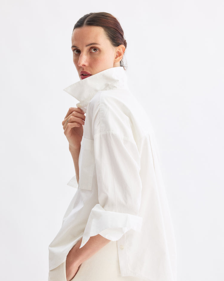 A person with dark hair pulled back wears the Arlo Mott Watts Side Button Shirt in White, collar turned up, and looks over their shoulder against a plain white background.