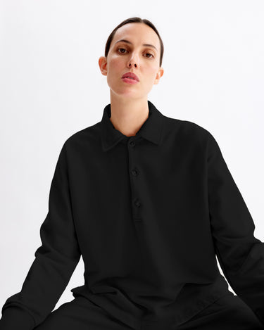 A person with short dark hair wears the Arlo Mott Elliott Polo Pullover in Black, sitting against a plain white background and looking directly at the camera with a neutral expression.