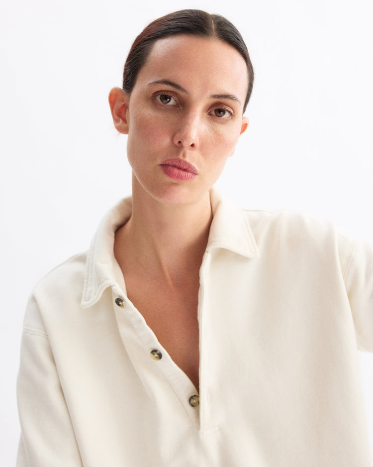A person with straight dark hair pulled back wears the Arlo Mott Elliott Polo Pullover in Chalk, looking directly at the camera with a neutral expression against a plain white background.
