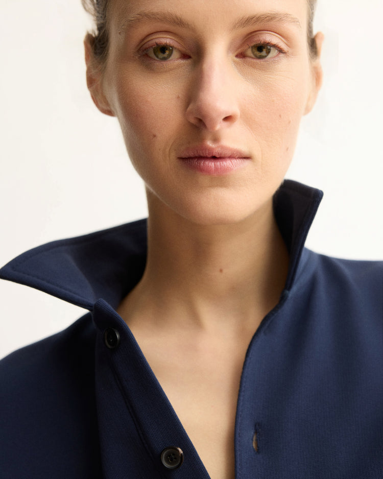 A person with light skin and hazel eyes wears the Arlo Mott Elliott Polo Pullover in Navy, collar turned up, looking confidently at the camera against a plain light background.