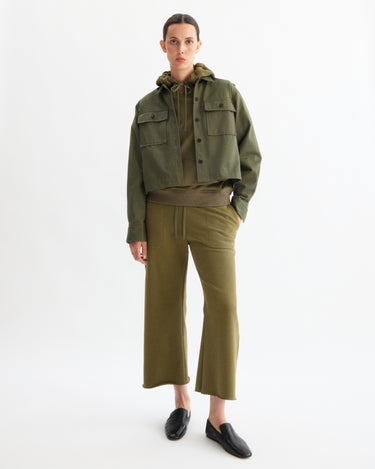 A person stands against a white background wearing Arlo Mott's Kane Cropped Wide Sweatpants in Olive with a matching jacket, hoodie, and black slip-on shoes.
