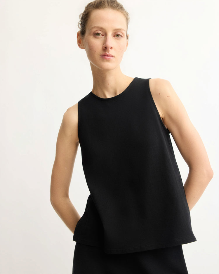 A person with light skin and light brown hair tied back wears the Arlo Mott Hart A-Line Swing Tank Top in Black with black bottoms, standing against a plain background and looking at the camera with a neutral expression.