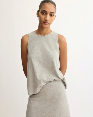 A woman with dark hair pulled back wears the Arlo Mott Hart A-Line Swing Tank Top in Grey, standing with her hands behind her back against a plain light background.