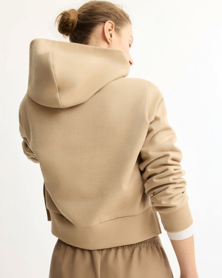 A person with light brown hair in a bun, facing away from the camera against a plain light background, wears the Arlo Mott Morris Hoodie With Snaps in Khaki and matching sweatpants.