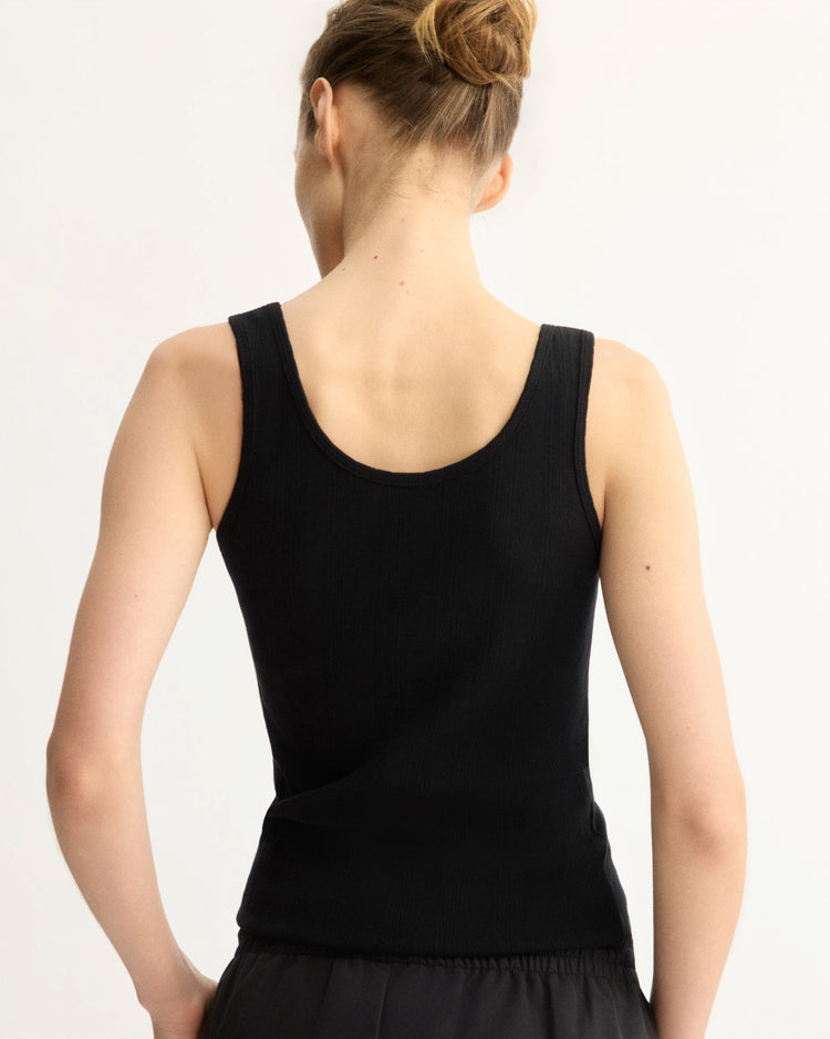 A woman with light skin and brown hair in a bun is shown from the back wearing the Arlo Mott Nevins Tank Top in Black with dark pants, posed against a plain light background.