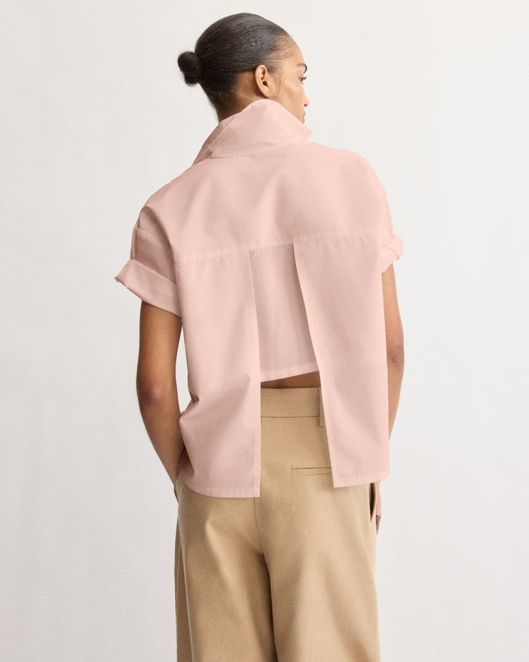 A person with hair in a bun wears the Arlo Mott Clark Split Back Top in Dusty Rose and tan high-waisted trousers, standing against a plain white background.