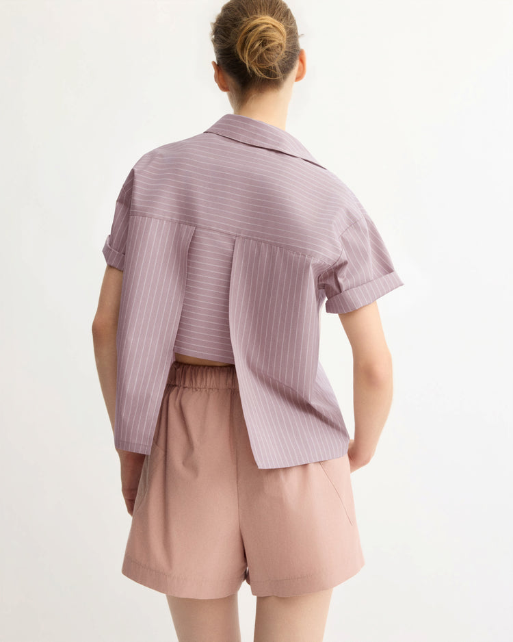A person with their hair in a bun is seen from behind, wearing the Arlo Mott Clark Split Back Top in Rose Stripe and light pink high-waisted shorts against a plain background.