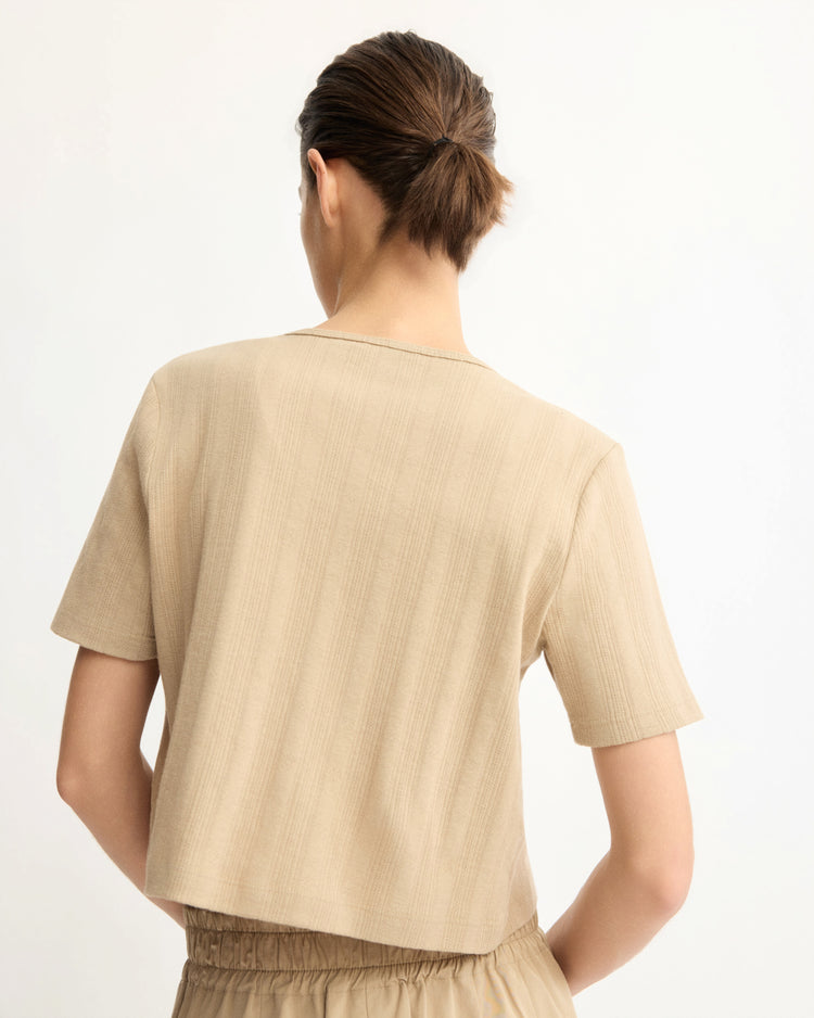 A person with short brown hair in a low bun is seen from behind, wearing the Arlo Mott Marion Short Sleeve Cardigan in Khaki and matching pants against a plain, light background.