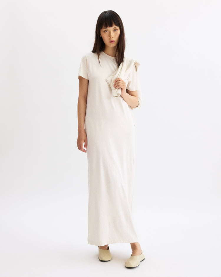 A woman with straight dark hair wears the Arlo Mott Hubert Short Sleeve Maxi Dress in Chalk and matching cream shoes, standing against a white background with a similar garment draped over her left arm.