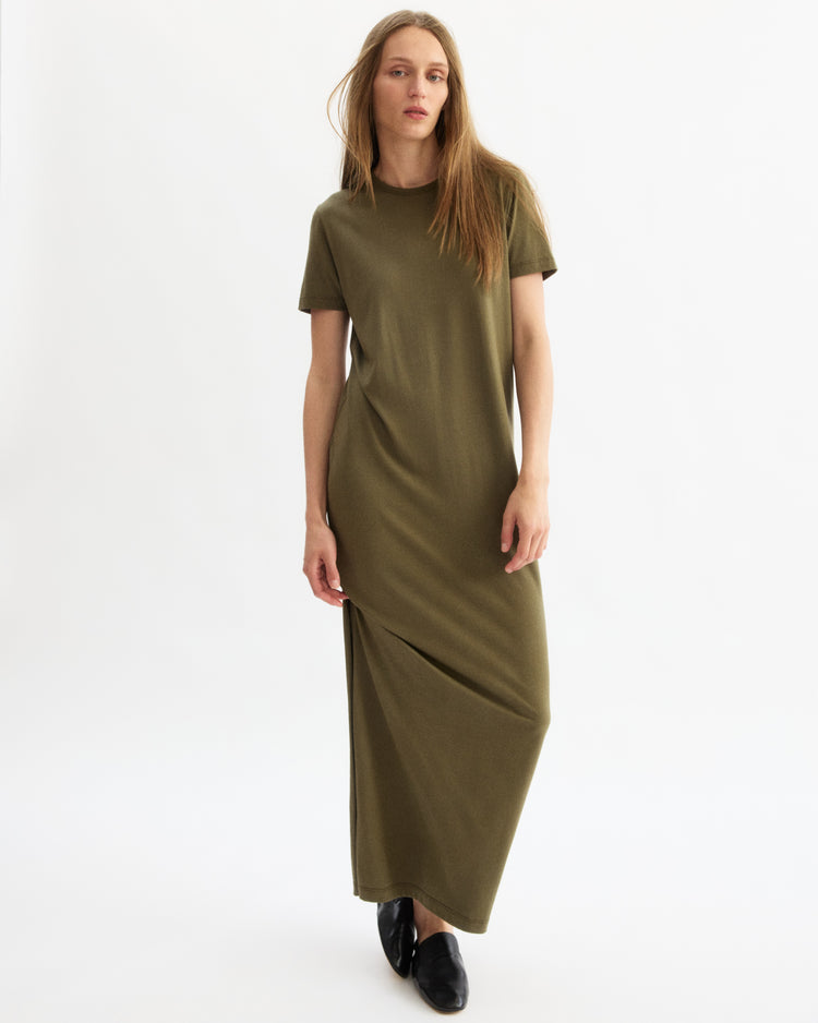 A woman with long, straight hair wears the Arlo Mott Hubert Short Sleeve Maxi Dress in Olive and black shoes, standing against a plain white background.