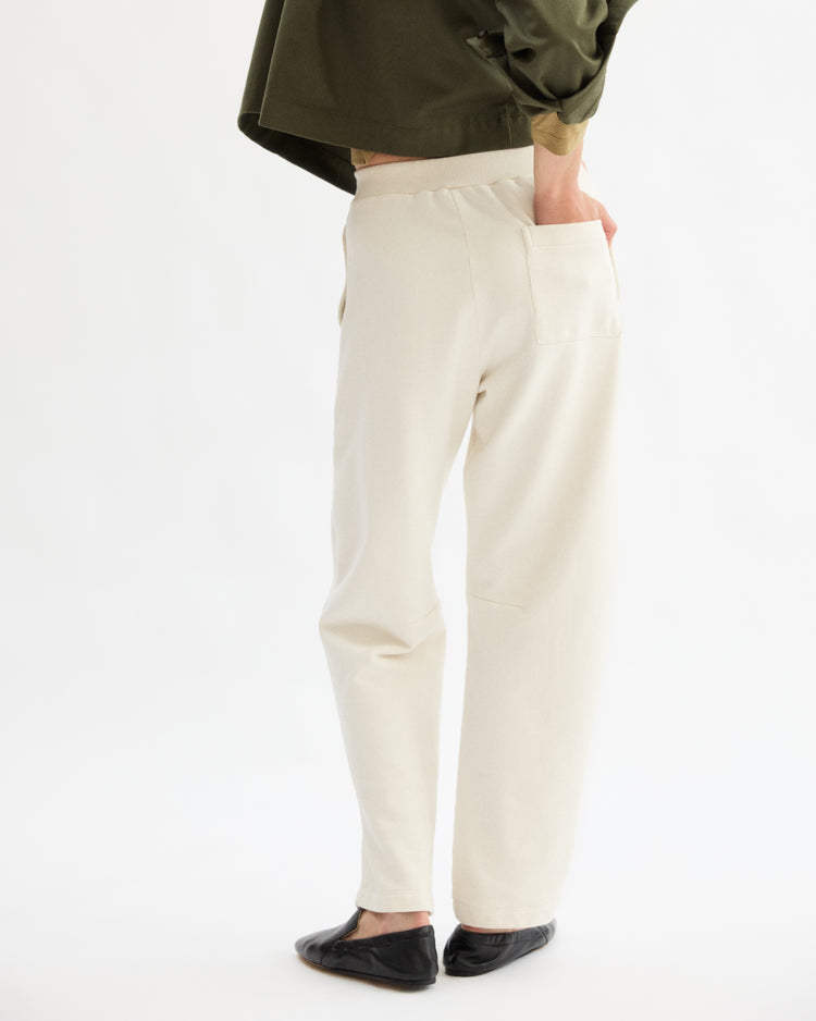 A person stands with their back turned, wearing Arlo Mott's Baltic Barrel Leg Sweatpants in Chalk, paired with a dark green top and black flats, one hand in the back pocket, against a plain white background.