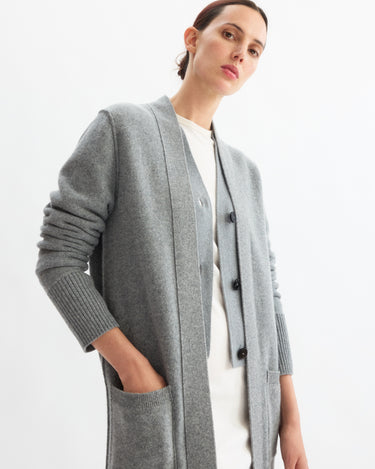 Wearing the Arlo Mott Sidney Duster Cardigan in Heather Grey over a white outfit, a person stands with hands in pockets, gazing slightly downward at the camera against a plain white background.