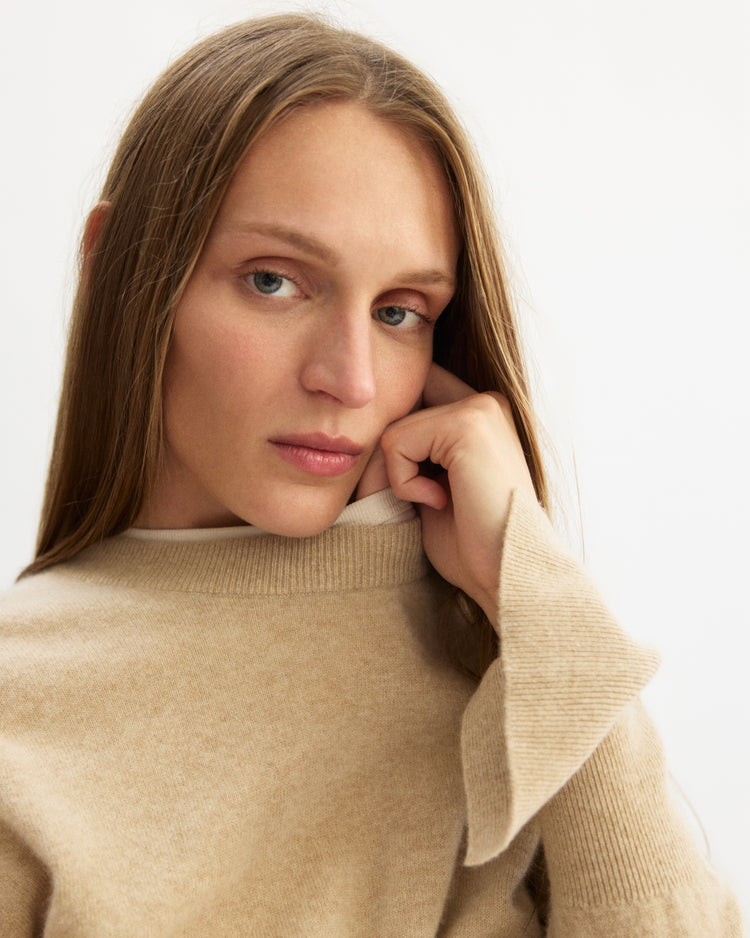 A woman with long hair wears an Arlo Mott Warren Classic Crew Neck sweater in oatmeal.