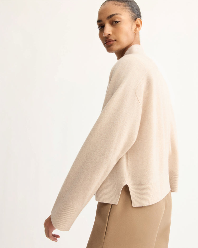 A person wearing the Arlo Mott Wooster Cardigan in Beige stands against a plain, light background, looking over their shoulder with a neutral expression.