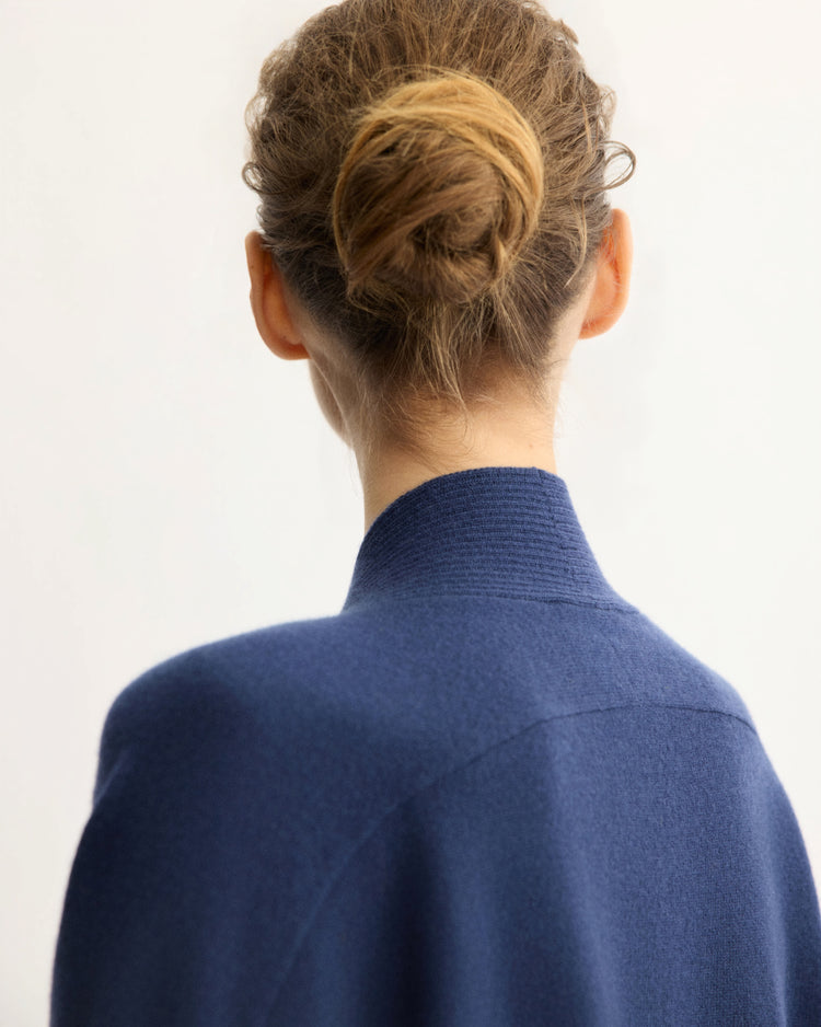 A person with light brown hair in a low bun, shown from the back, wears the Arlo Mott Wooster Cardigan in Navy against a plain light background.
