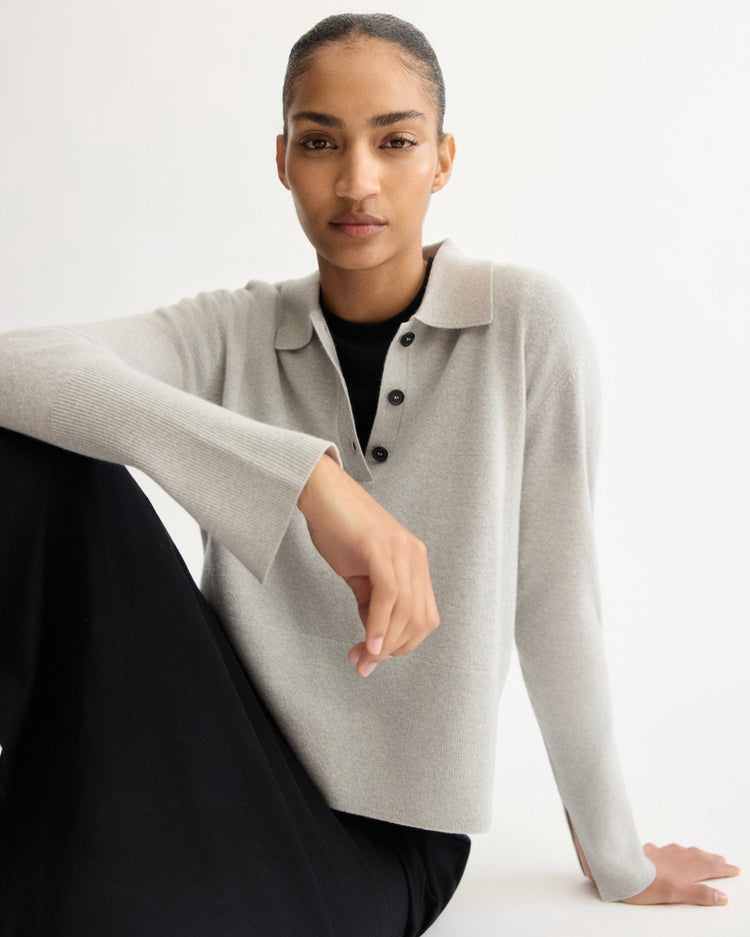 A person with neatly tied-back hair wears the Arlo Mott Berry Polo Long Sleeve in Grey and black pants, sitting against a white background and looking confidently at the camera.