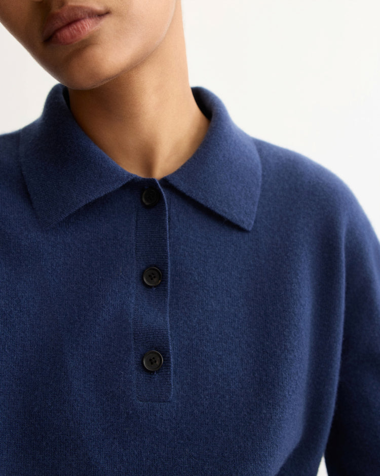 A person wears the Arlo Mott Berry Polo Long Sleeve in Navy, a dark blue collared sweater with three black buttons, shown from the shoulders up against a plain light background.