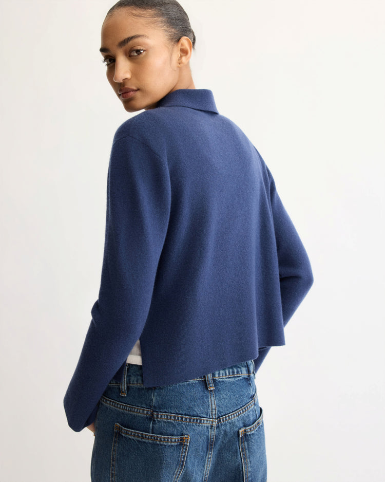 Wearing the Arlo Mott Berry Polo Long Sleeve in Navy and blue jeans, a person with hair pulled back stands with their back to the camera, turning their head to look over their shoulder.