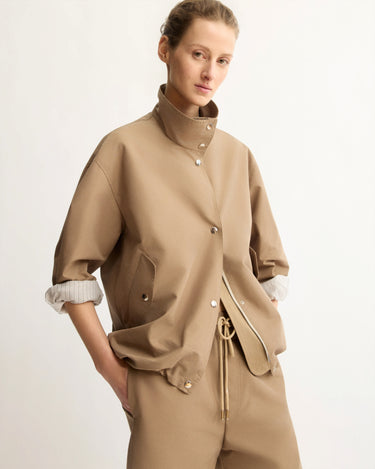 A person stands against a plain background wearing the Arlo Mott Logan Tech Jacket in Khaki with rolled-up sleeves and matching pants, hands in pockets, looking confidently at the camera.
